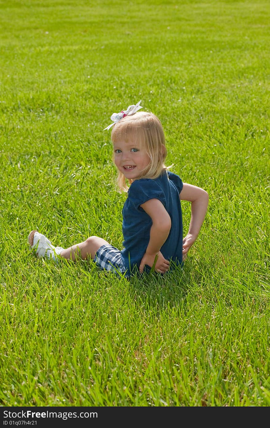 Little blond girl sitting in grass turning to smile at camera. Little blond girl sitting in grass turning to smile at camera