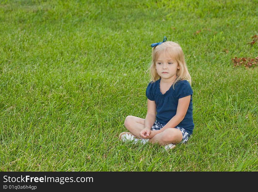 One blond girl sitting in grass with a contemplative look on her face. One blond girl sitting in grass with a contemplative look on her face