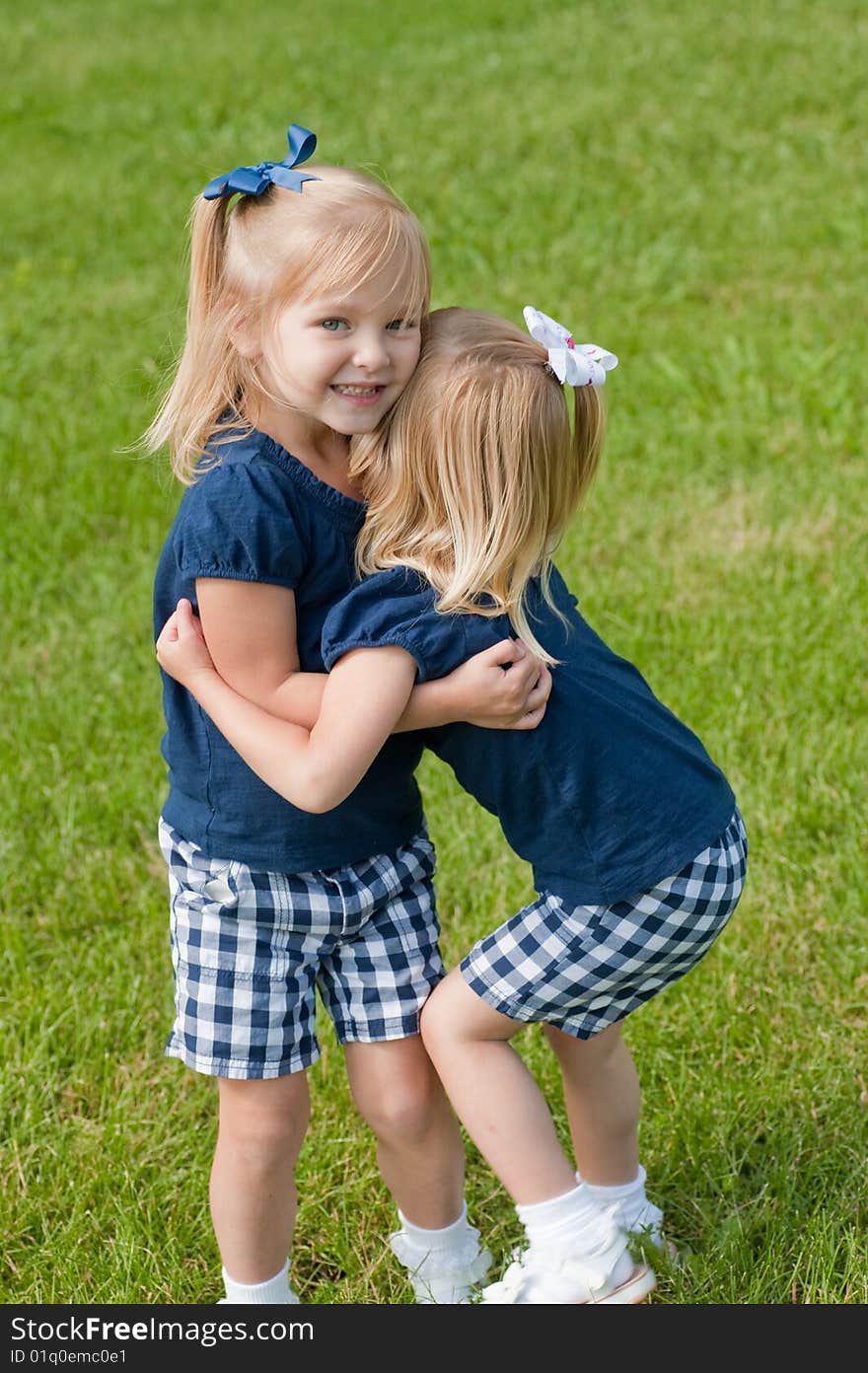 Two little blond girls in grass hugging each other. Two little blond girls in grass hugging each other