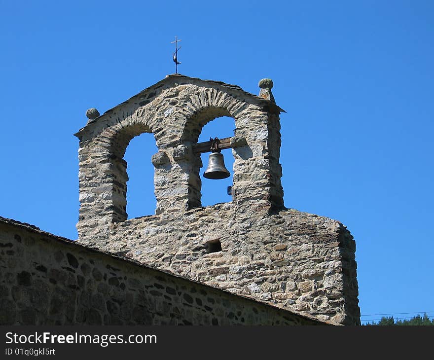 Stone belltower with single bell against clear blue sky