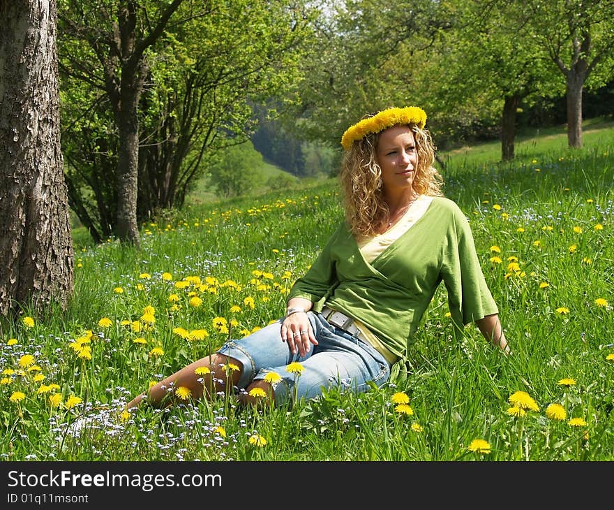 Curly girl with dandelion chain on head sitting in orchard