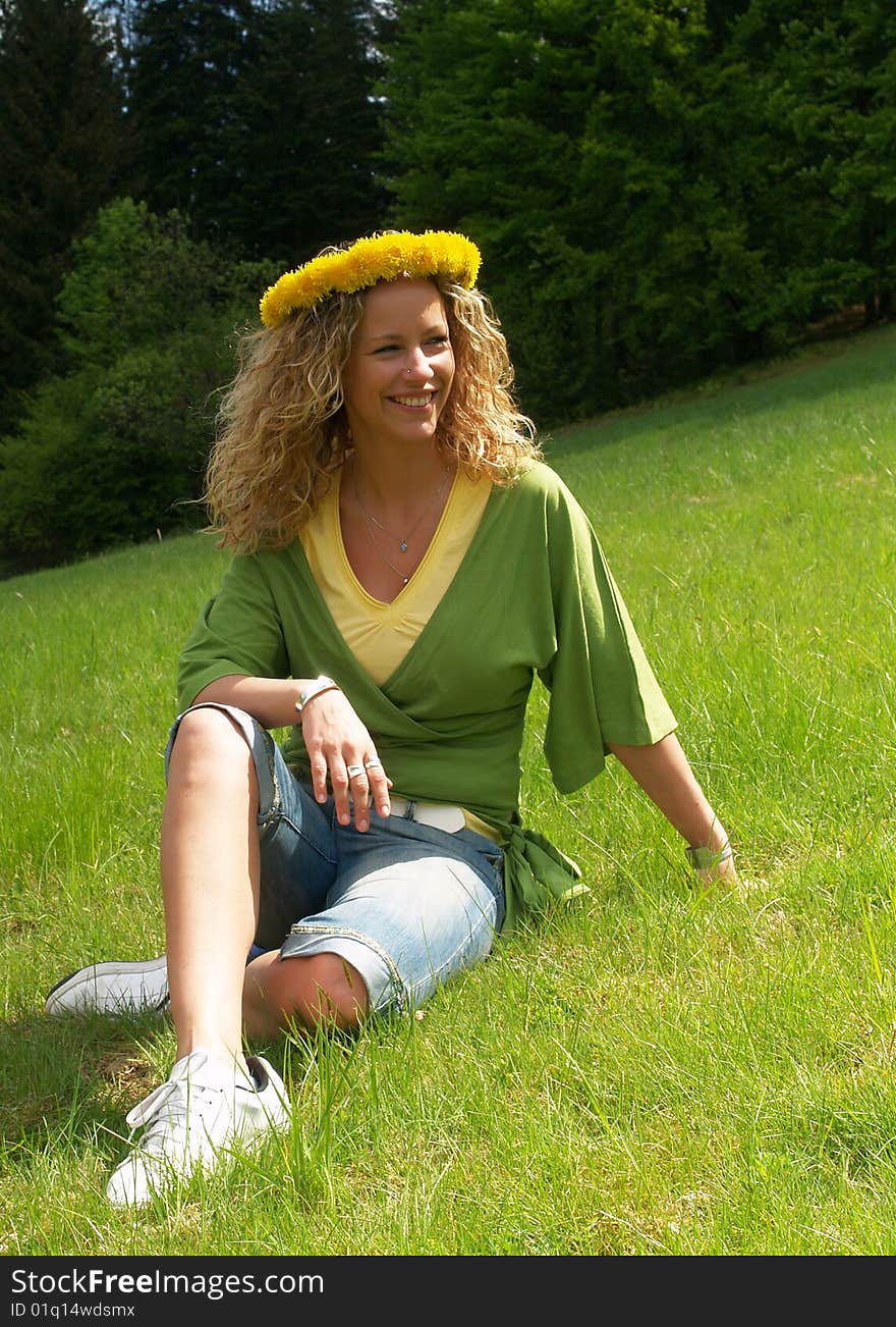 Curly girl with dandelion chain on head sitting on meadow