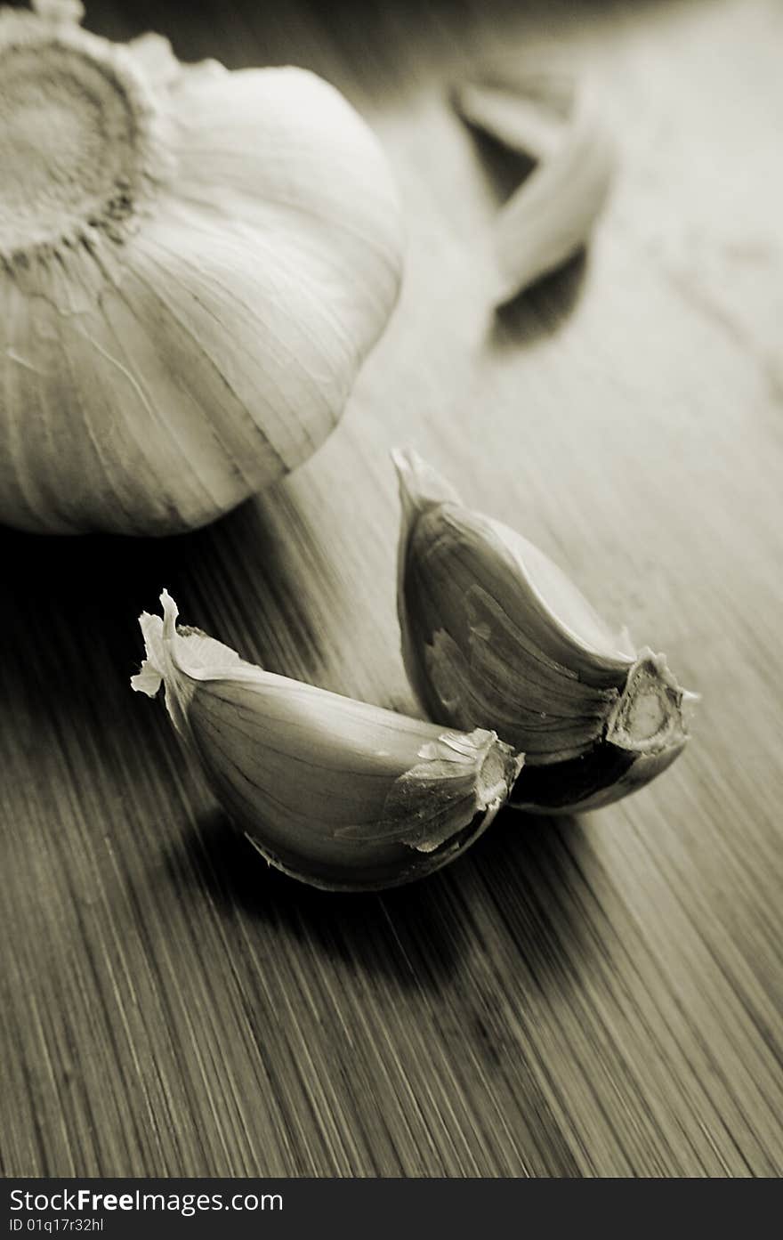 Garlic bulb and its slices on wooden texture, sepia