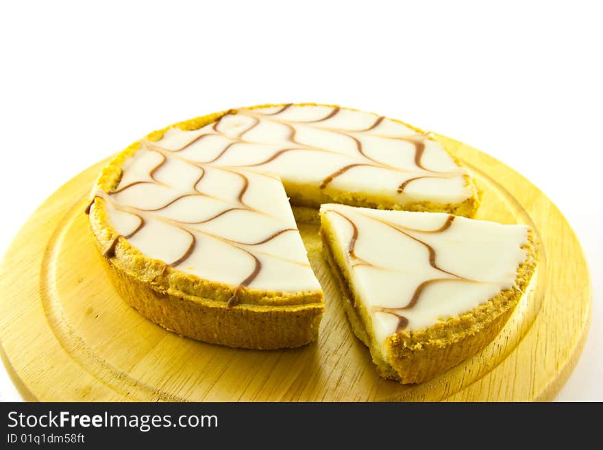 Delicious looking iced bakewell tart on a wooden platter with a plain background