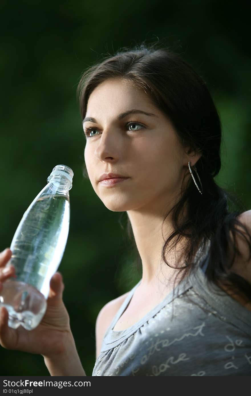 Beautiful young woman in the park. Drinks water.