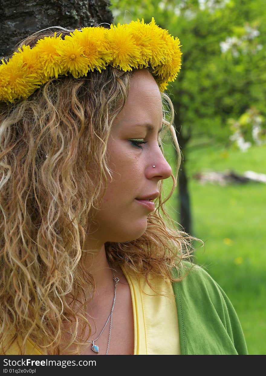 Curly girl with dandelion chain on head standing by birch tree