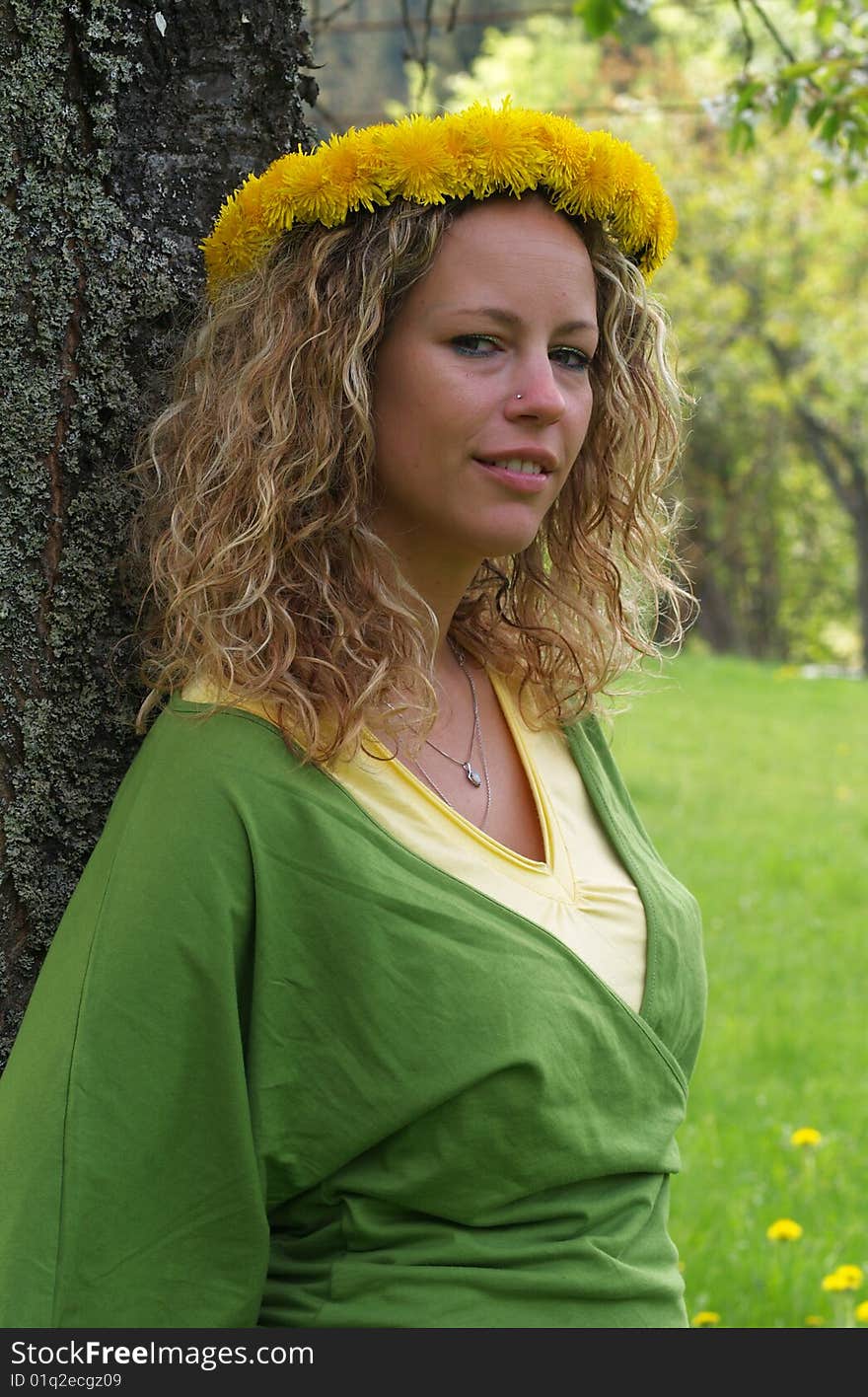 Curly girl with dandelion chain on head standing by birch tree