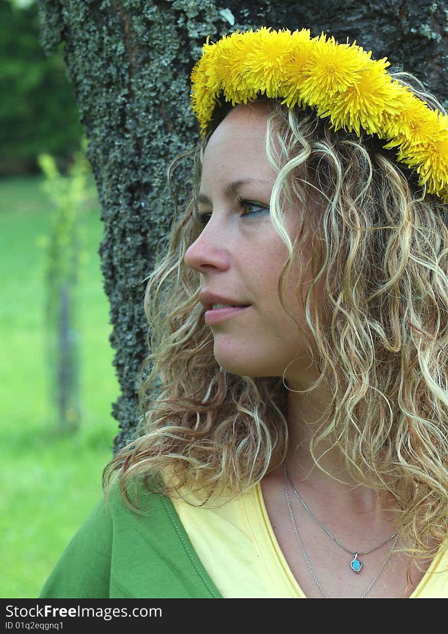 Curly girl with dandelion chain on head standing by birch tree