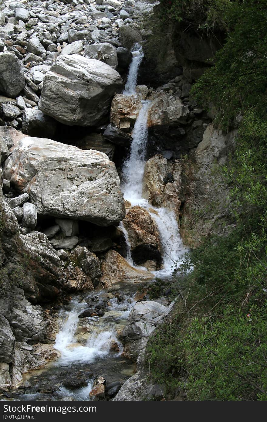 Brook falling in stages between rocks and pebbles in valley. Brook falling in stages between rocks and pebbles in valley