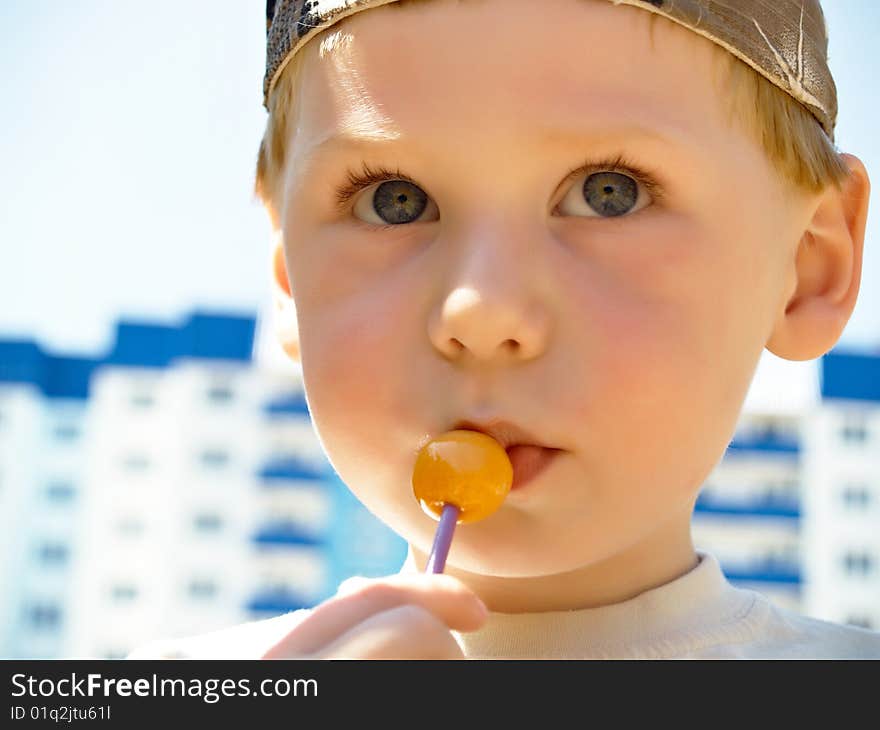 The little boy with a sweet in a hand costs in the street. The little boy with a sweet in a hand costs in the street