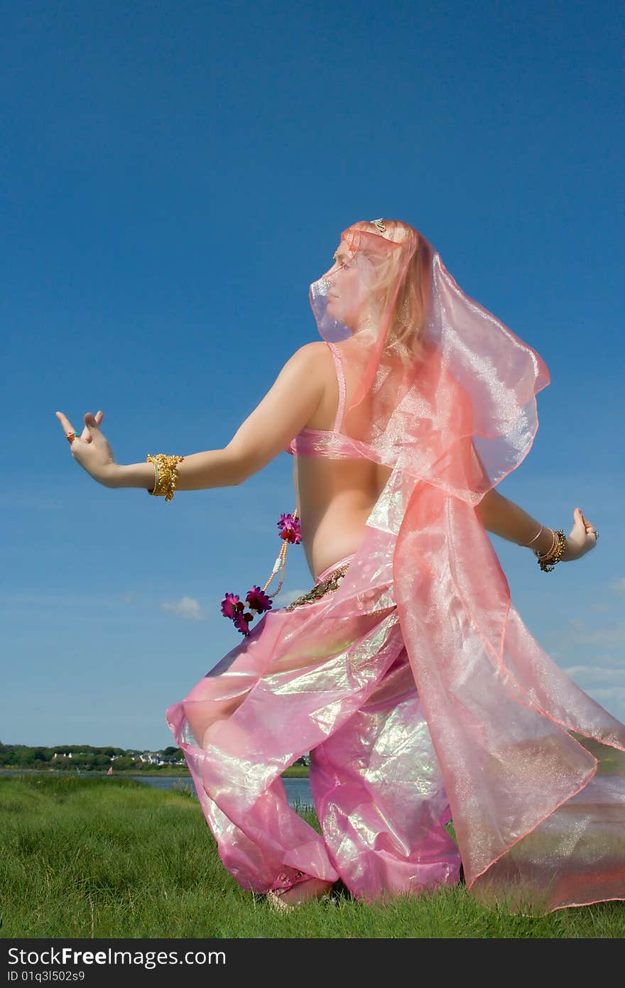 A woman in pink asian dress dancing on the grass and a blue sky. A woman in pink asian dress dancing on the grass and a blue sky