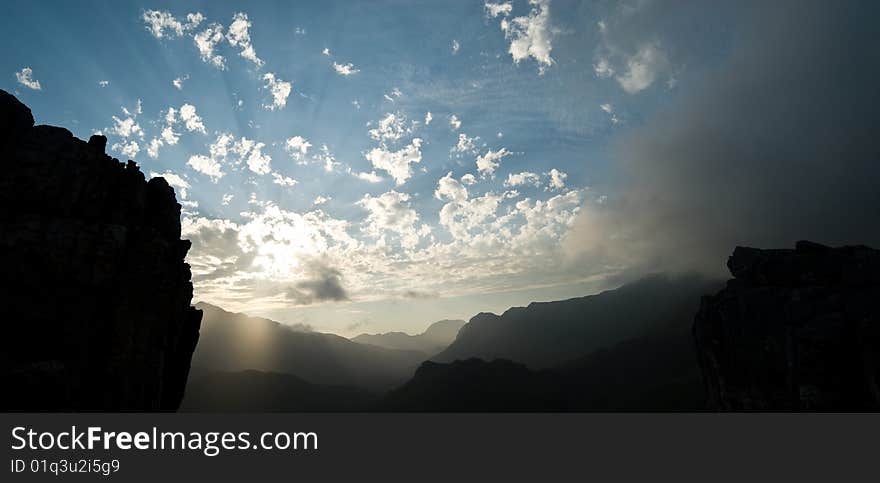 Sun rays breaking through clouds with mountains in foreground. Sun rays breaking through clouds with mountains in foreground