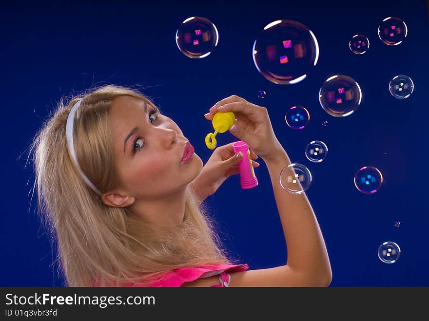 Young beautiful blond inflate soap bubbles on a blue background