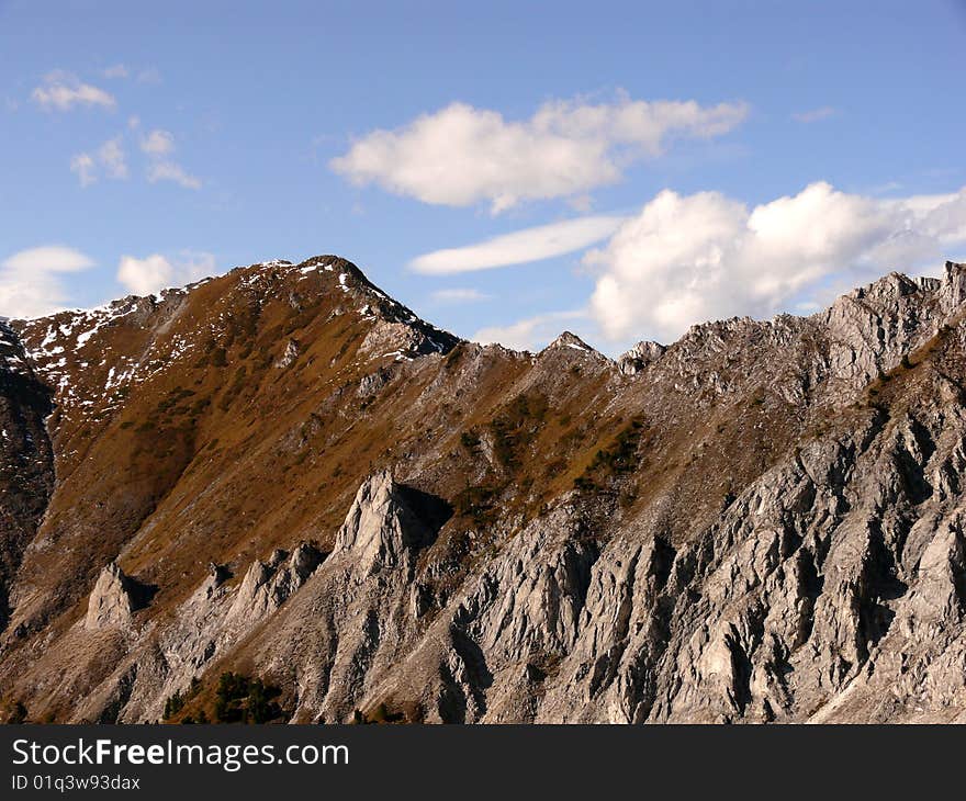 Clouds fly over the beautiful peaks of mountains in the background of blue sky. Clouds fly over the beautiful peaks of mountains in the background of blue sky