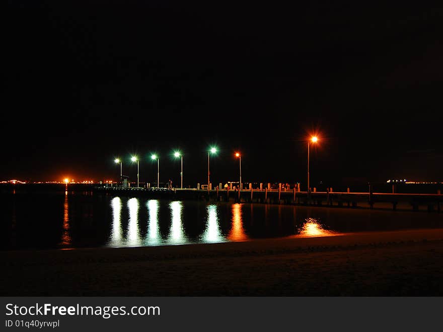 Rockingham jetty at night, waters of the ocean reflecting the green and red lights on the jetty. Fishermen come there every night to catch fish seeking shelter under the jetty.