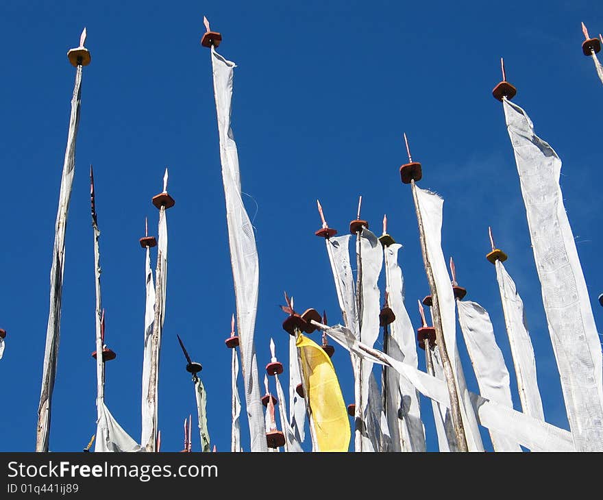 Prayer flag poles with printed flags cob=ntaining religious mantra, against a blue sky. Prayer flag poles with printed flags cob=ntaining religious mantra, against a blue sky