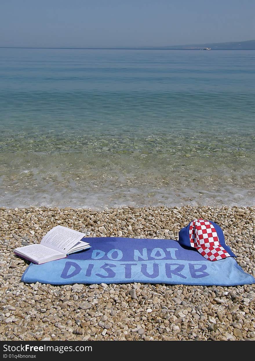 Towel do not disturb with book and cap at beach near the Adriatic sea - Croatia (Dalmatia). Towel do not disturb with book and cap at beach near the Adriatic sea - Croatia (Dalmatia)