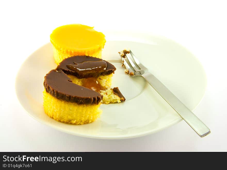 Two delicious looking cup cakes with a treacle drizzle resting on a white plate with a fork on a plain background. Two delicious looking cup cakes with a treacle drizzle resting on a white plate with a fork on a plain background