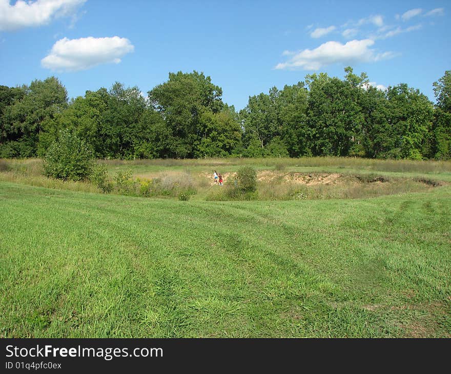 Children playing in the far distance in a large ditch, near a forest, in a meadow. Children playing in the far distance in a large ditch, near a forest, in a meadow.