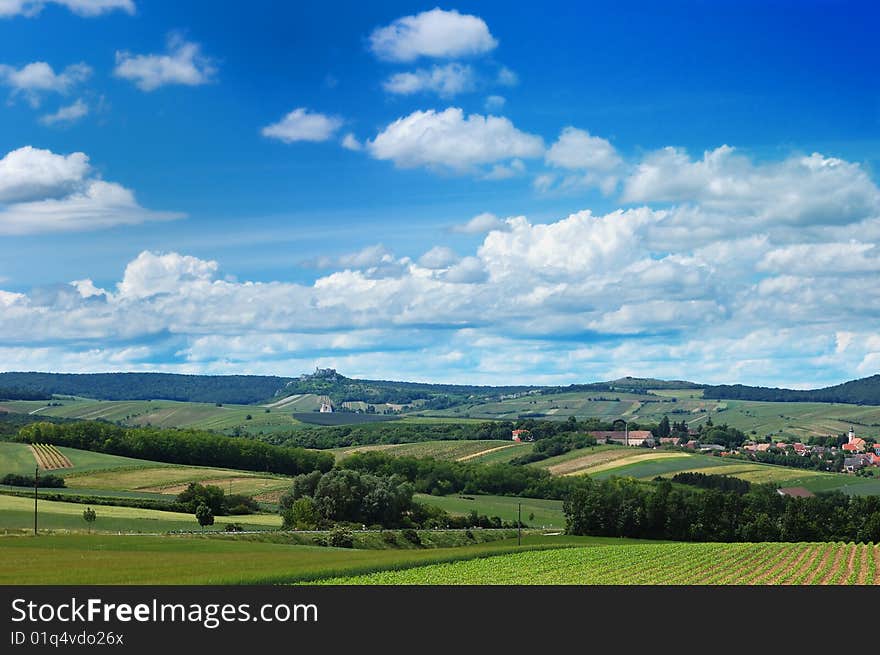 Rural landscape with a cozy village among the hills, fields and meadows under cloudy blue sky. Rural landscape with a cozy village among the hills, fields and meadows under cloudy blue sky