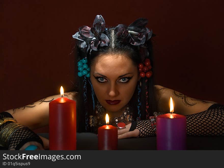 Young beautiful soothsayer with three candles on dark red background. Young beautiful soothsayer with three candles on dark red background