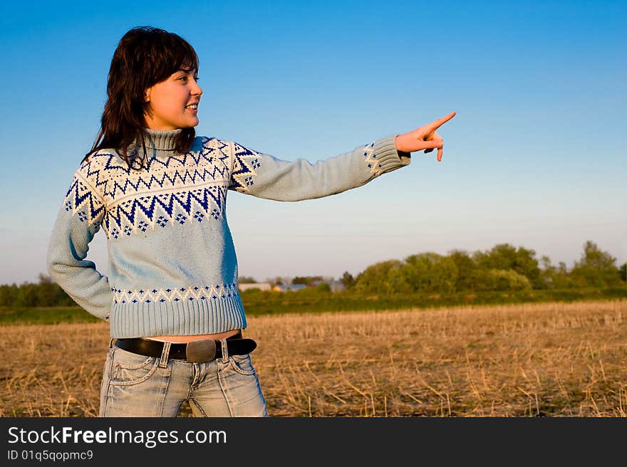 Smiling girl showing with finger. Outdoors with a field in the background