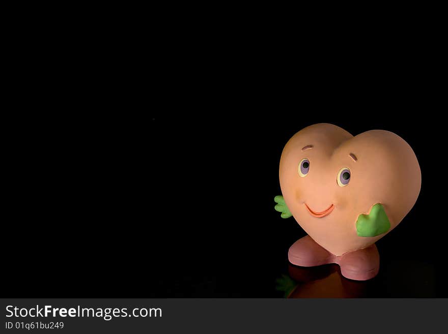 Cute heart-shaped doll showing the thumbs-up sign, isolated against black background with copy space on the left and above. Cute heart-shaped doll showing the thumbs-up sign, isolated against black background with copy space on the left and above