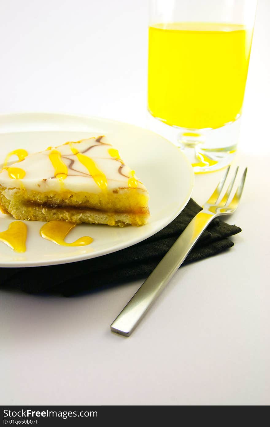 Delicious looking iced bakewell tart on a black plate with a treacle drizzle and a fork on a plain background