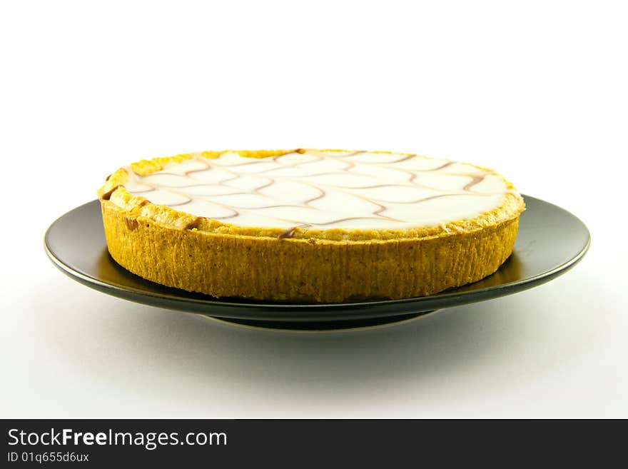 Delicious looking iced bakewell tart on a black plate with a plain background