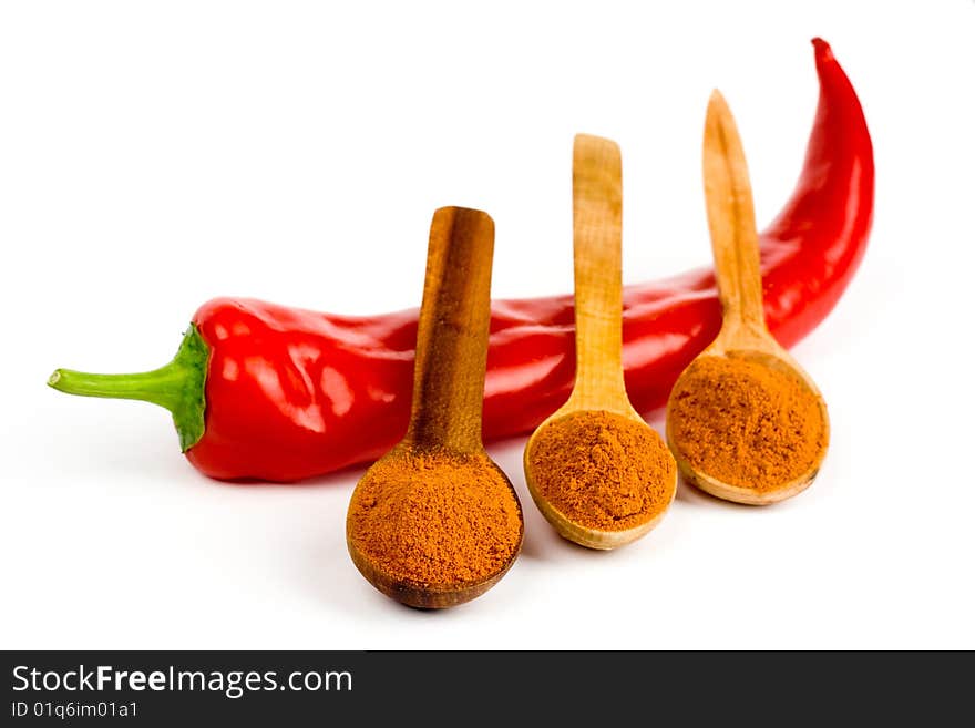 A composition of a pod of red hot  pepper and three wooden spoonful of ground red pepper on a white background. A composition of a pod of red hot  pepper and three wooden spoonful of ground red pepper on a white background