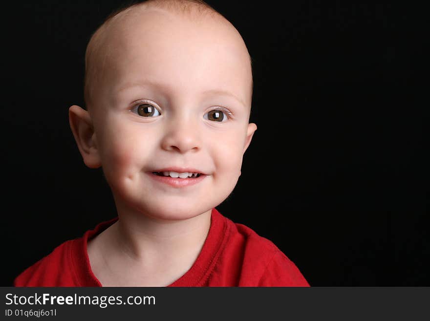 Blonde toddler against a black background with a big smile