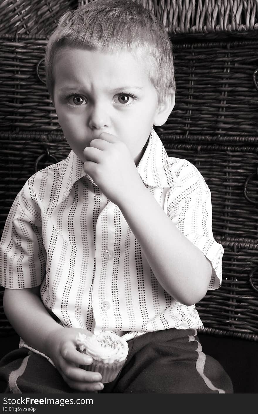 Serious toddler eating a cup cake, sitting against drawers