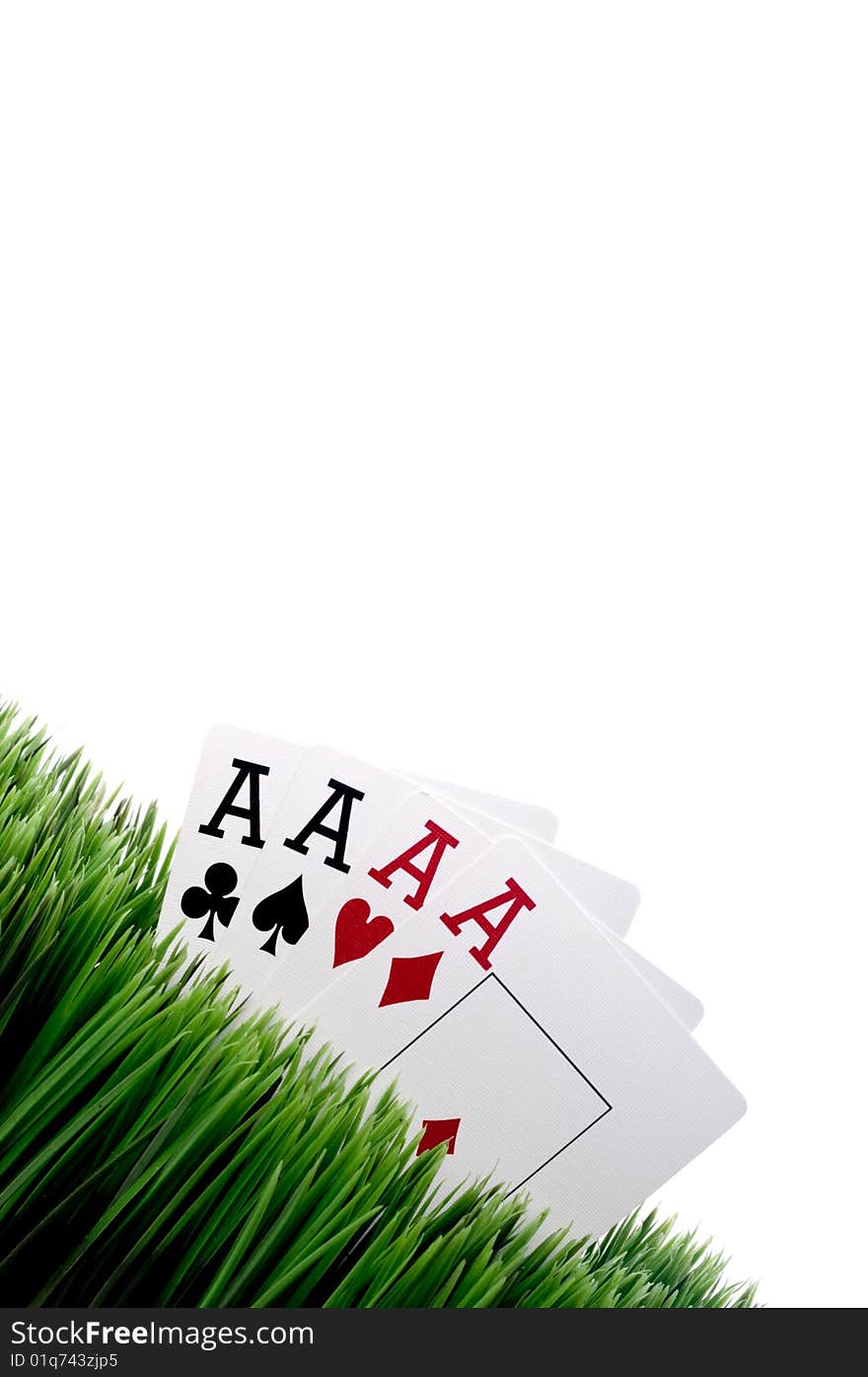 A tilted image of four ace playing cards in grass with a white background