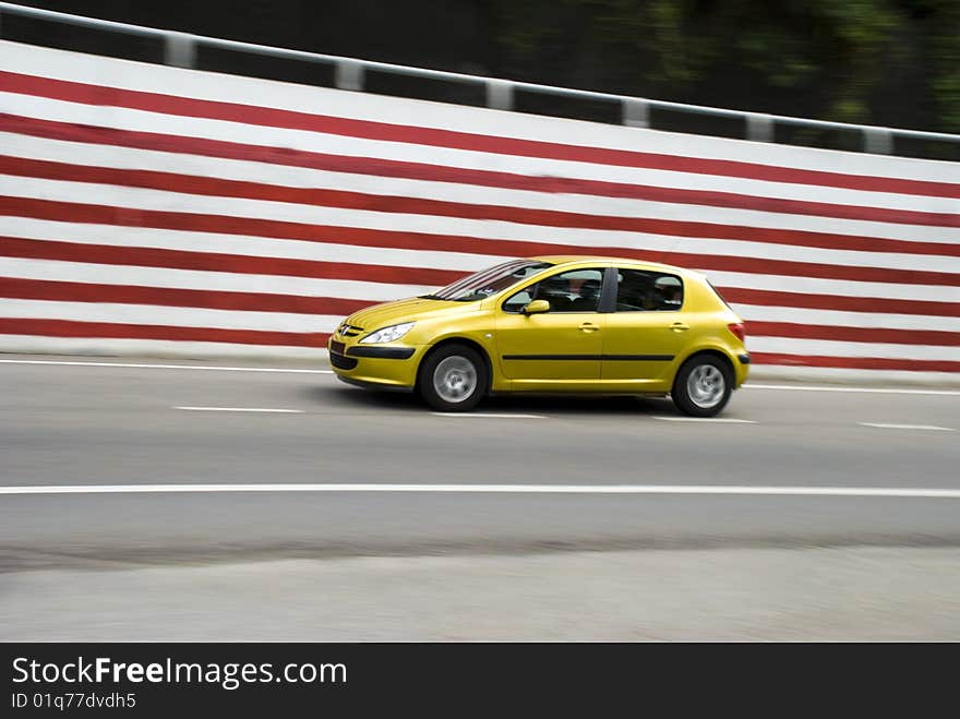 A small yellow car with some motion blur being driven next to a red and wall. ADOBE RGB color profile. A small yellow car with some motion blur being driven next to a red and wall. ADOBE RGB color profile