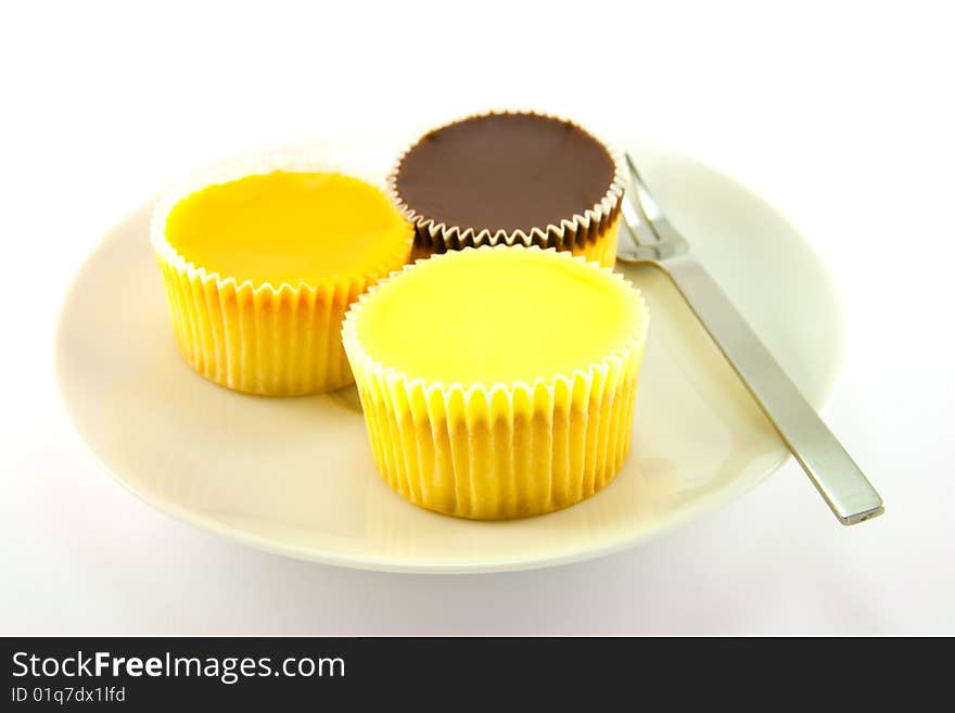 Three delicious looking cup cakes resting on a white plate with a fork on a plain background. Three delicious looking cup cakes resting on a white plate with a fork on a plain background