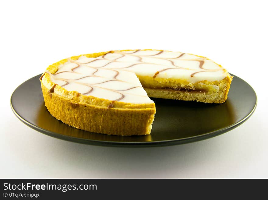 Delicious looking iced bakewell tart on a black plate with a plain background