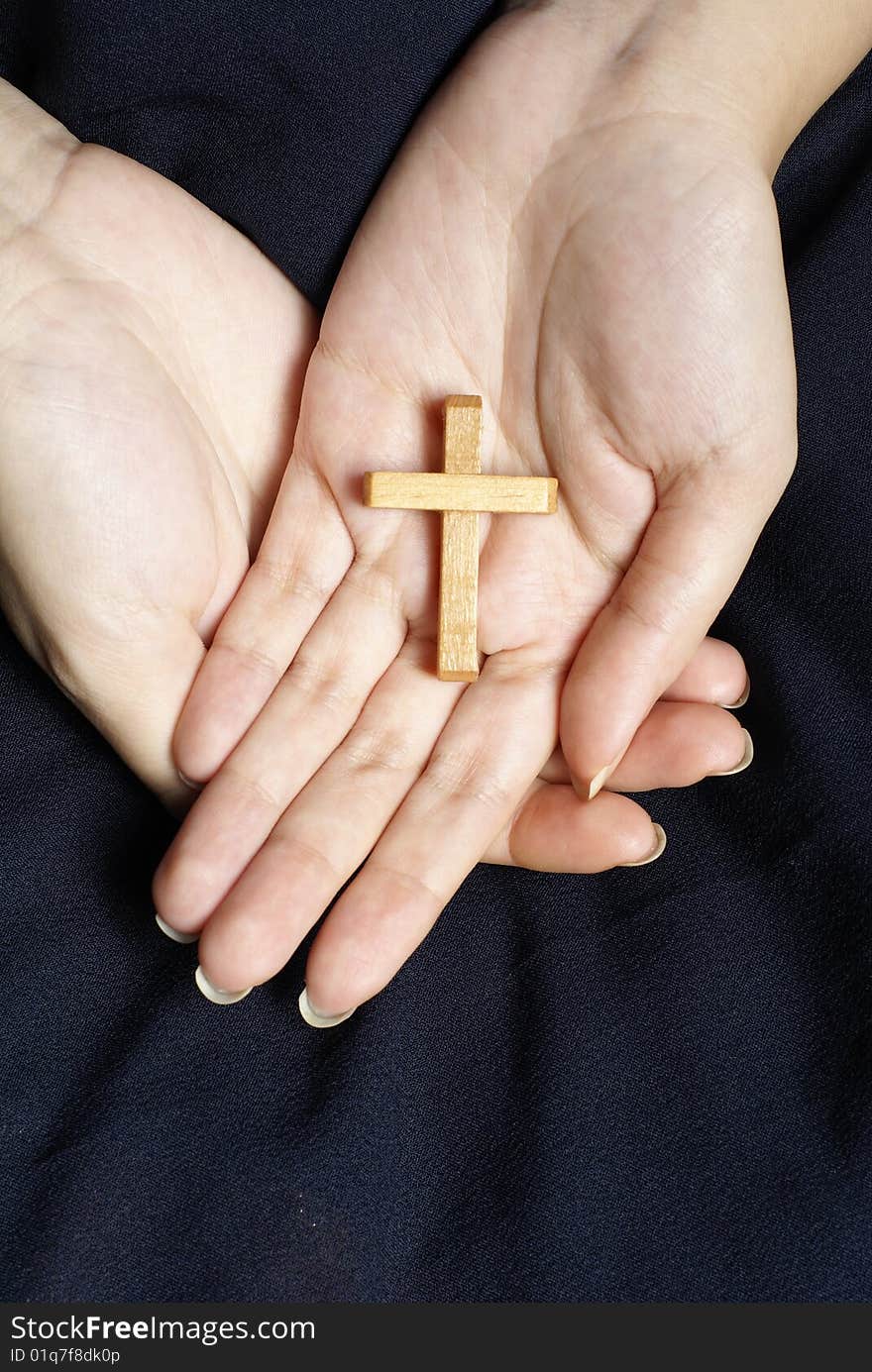 Wooden cross in female hands on dark blue cloth  background