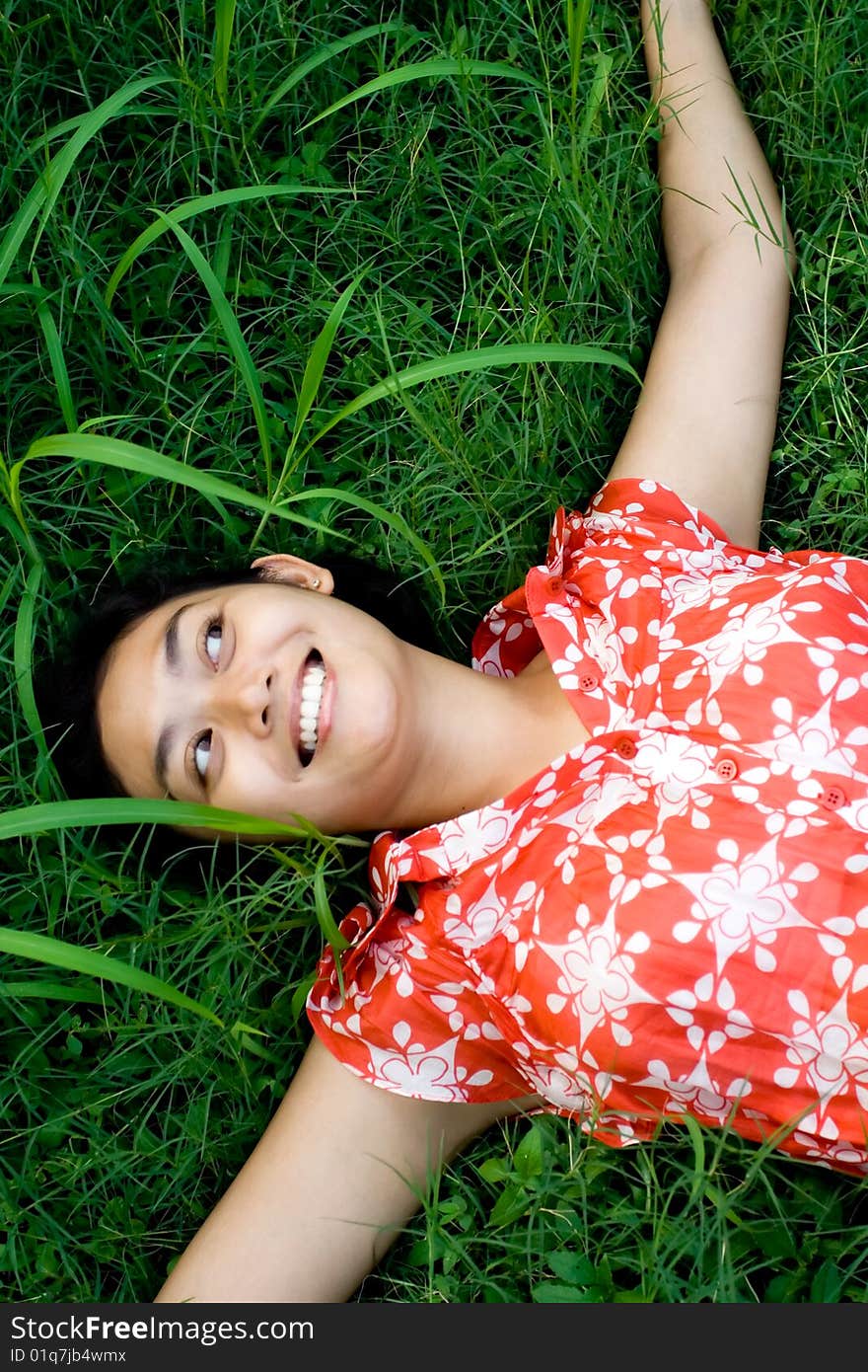 Happy asian woman laying on green grass seems to enjoy a beautiful day in nature. Happy asian woman laying on green grass seems to enjoy a beautiful day in nature.