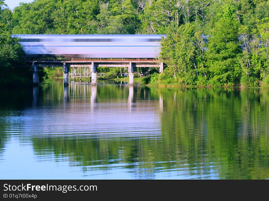 A train speeding across a train bridge over a creek, making reflections in the light of the sunrise. A train speeding across a train bridge over a creek, making reflections in the light of the sunrise.