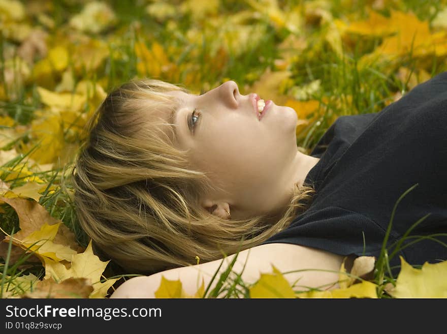 Young girl lying on the grass in the autumn leaves, and look up