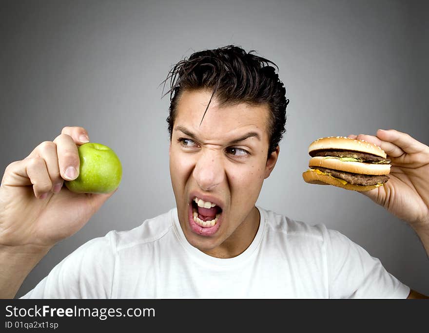 Man holds apple and burger while looking agitated. Man holds apple and burger while looking agitated