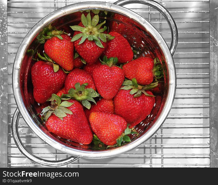 Freshly rinsed strawberries in a stainless steel strainer.