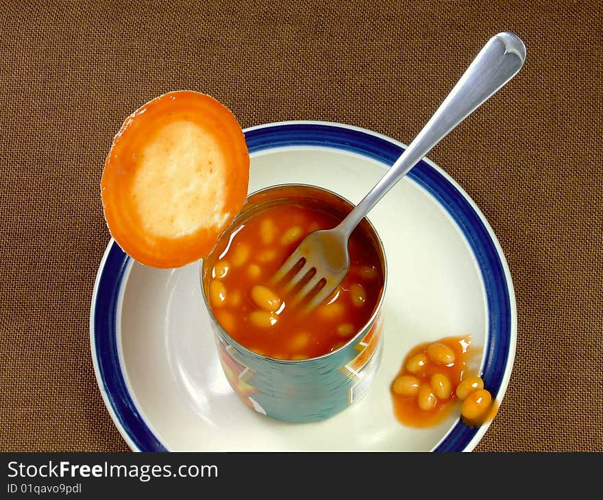 An opened tin of baked beans, with fork, sitting on a plate. An opened tin of baked beans, with fork, sitting on a plate.