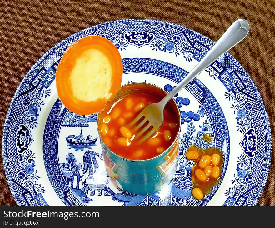 An opened tin of baked beans, with fork, sitting on a dinner plate. An opened tin of baked beans, with fork, sitting on a dinner plate.