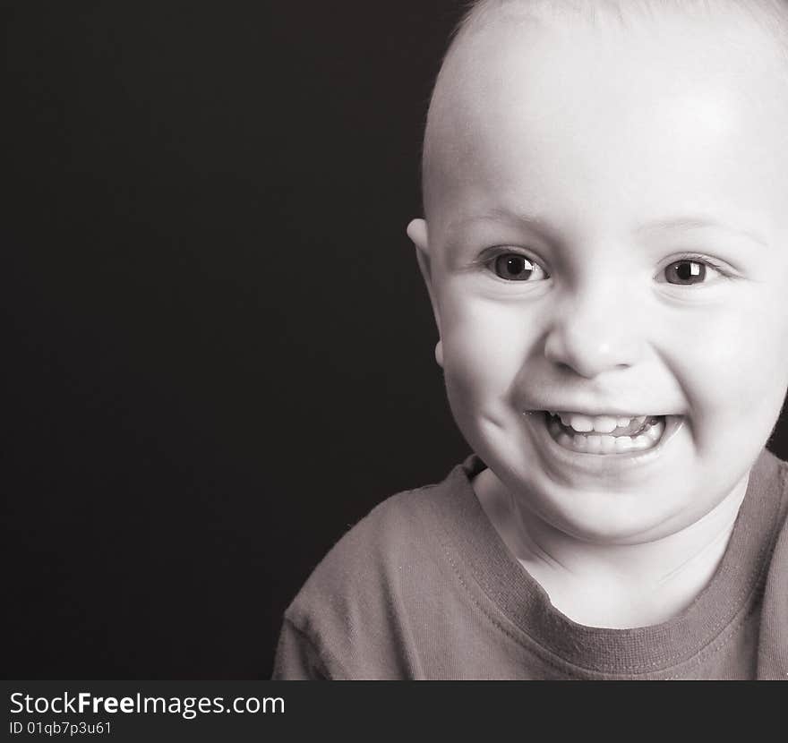 Blonde toddler against a black background with a big smile