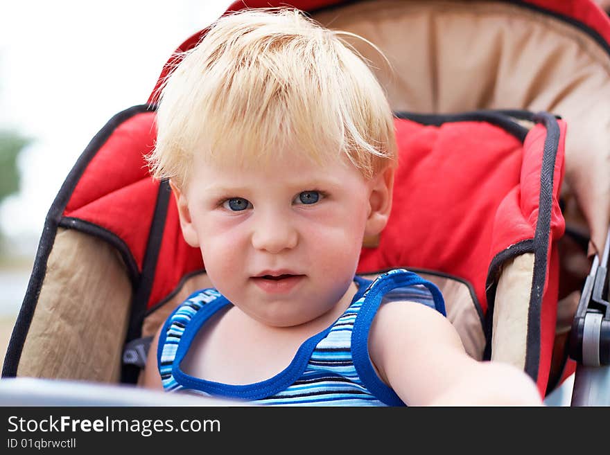 The little boy sits in a children s carriage