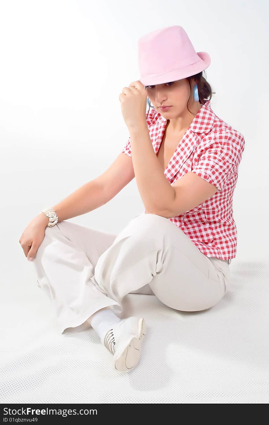 A nice young woman in a hat sitting with legs crossed, on white background. A nice young woman in a hat sitting with legs crossed, on white background