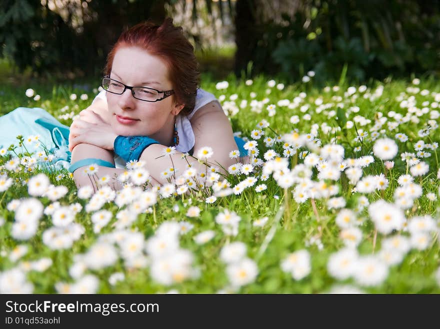 Young woman with glasses laying on grass in park full of small white flowers. Young woman with glasses laying on grass in park full of small white flowers.