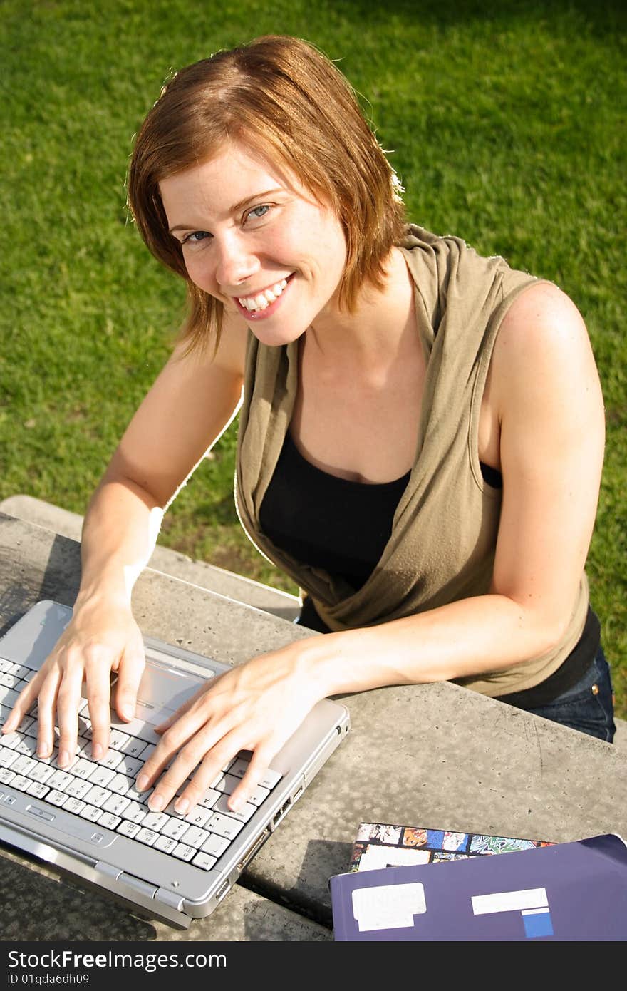 A female student typing on her laptop computer at a picnic table on campus. A female student typing on her laptop computer at a picnic table on campus