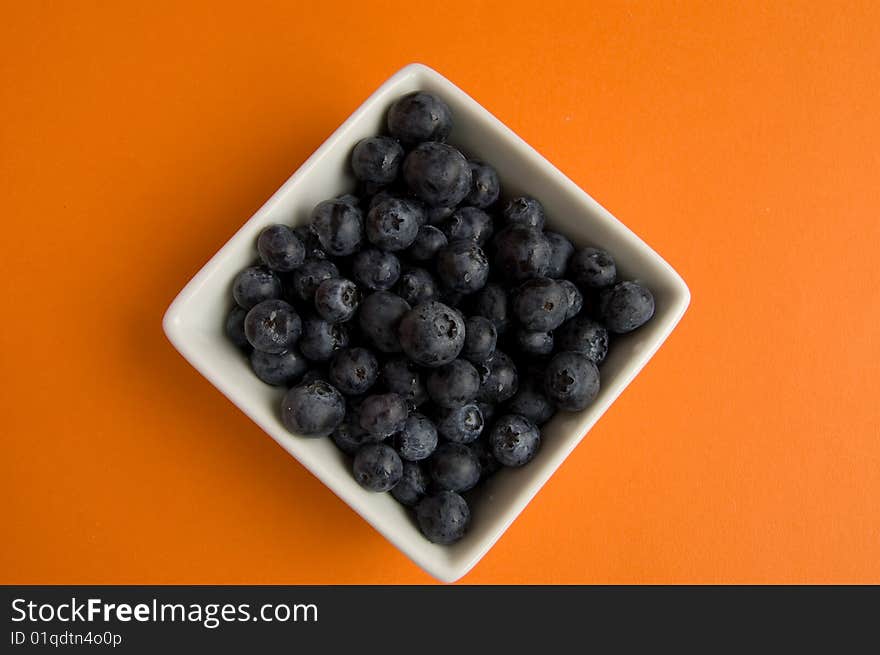 Fresh blueberries in square white bowl on orange background